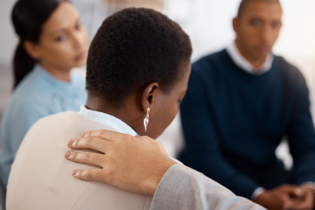 Mental health, support and black woman in a counseling therapy session with a group of people helping with stress. Meeting, anxiety and depressed employee sad in debt, grief and depression at work.